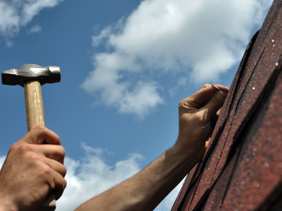 Roofer doing roof repair with a hammer on shingles