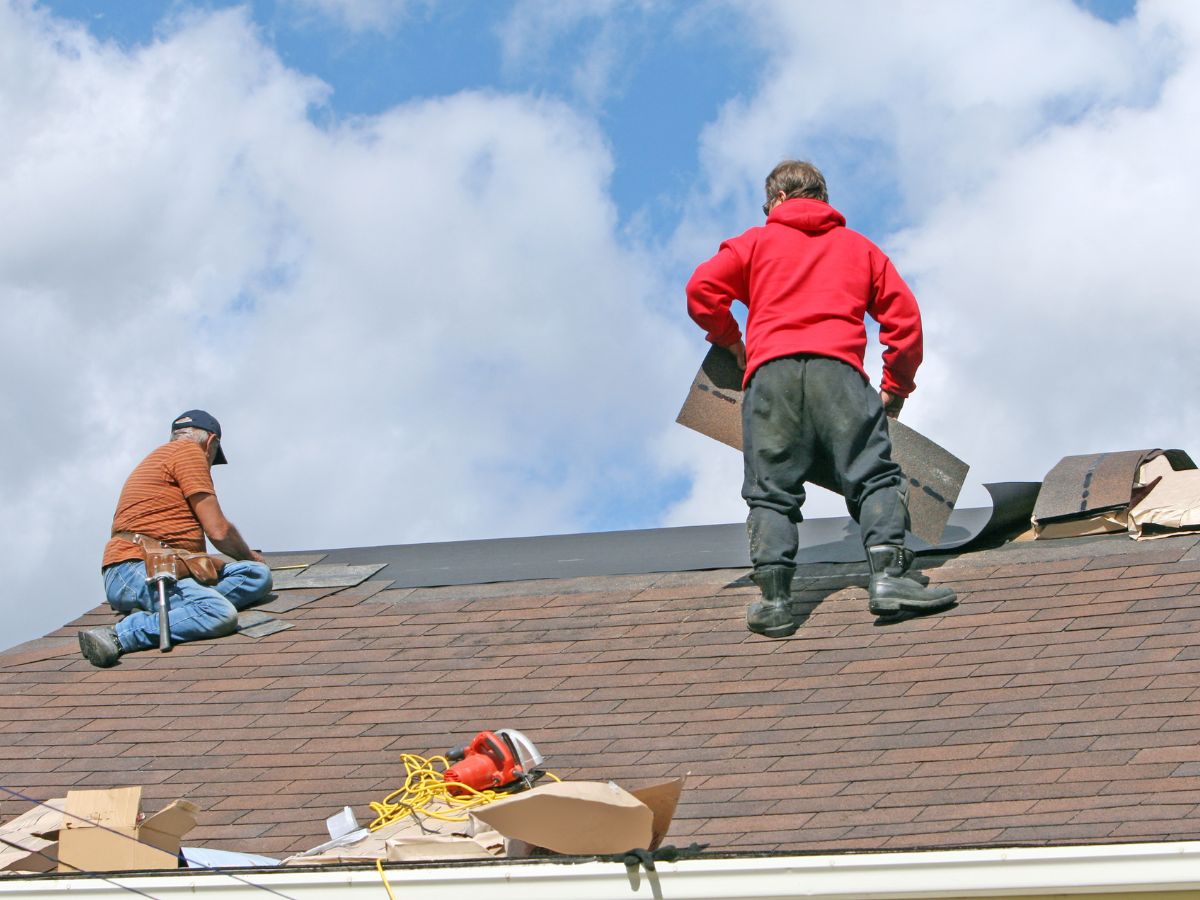 Roofers replacing missing shingles on a steep rooftop
